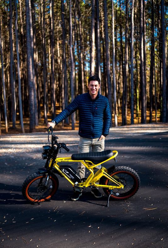 Rider with a yellow fat-tire e-bike on a pine-lined road
